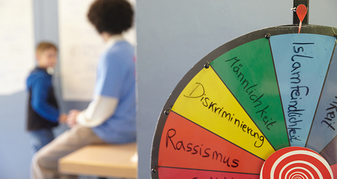 Eine Drehscheibe mit Begriffen wie Rassismus und Diskriminierung, zwei Jungs im Hintergrund